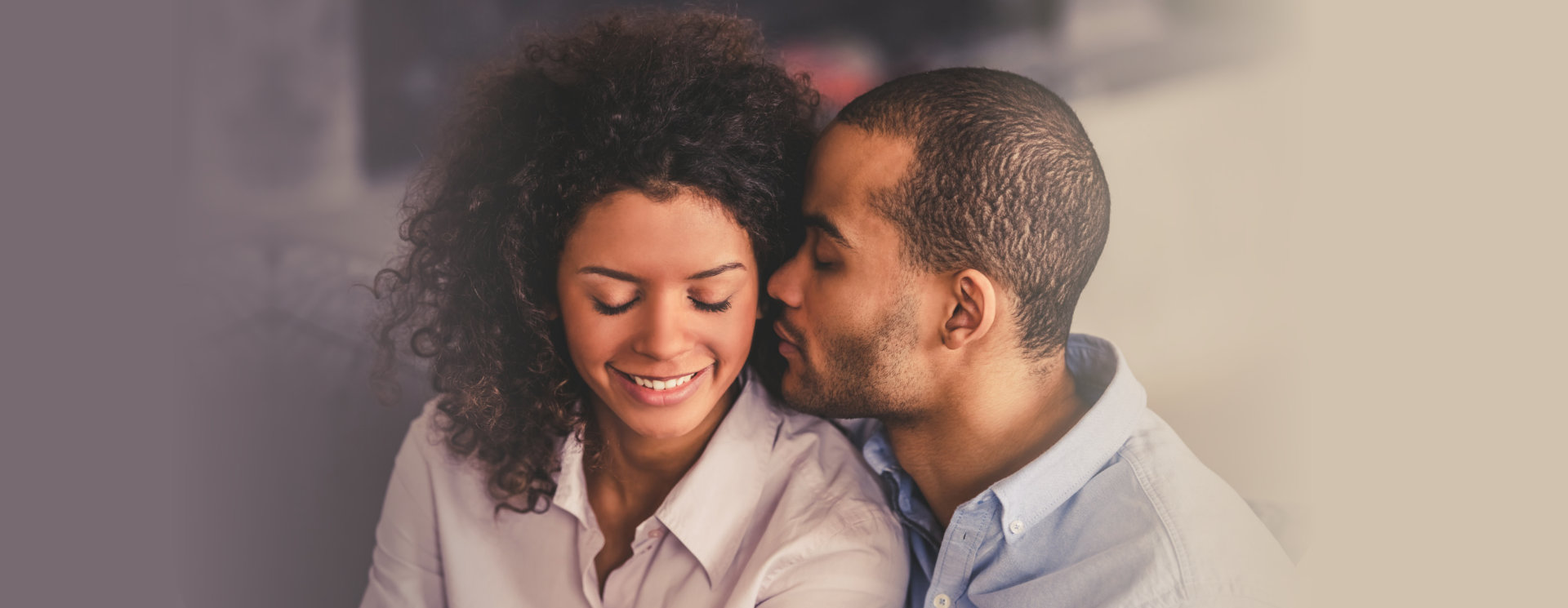 Beautiful young Afro American couple is hugging and smiling while sitting together on couch at home